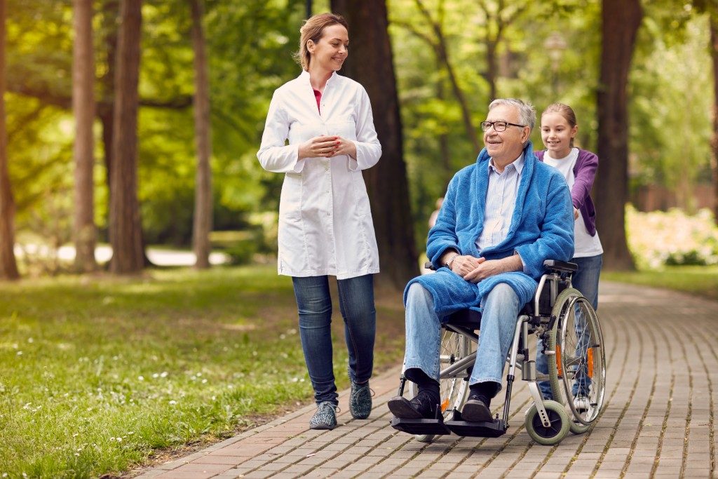 elderly man on wheelchair with caregiver nurse and granddaughter outdoor