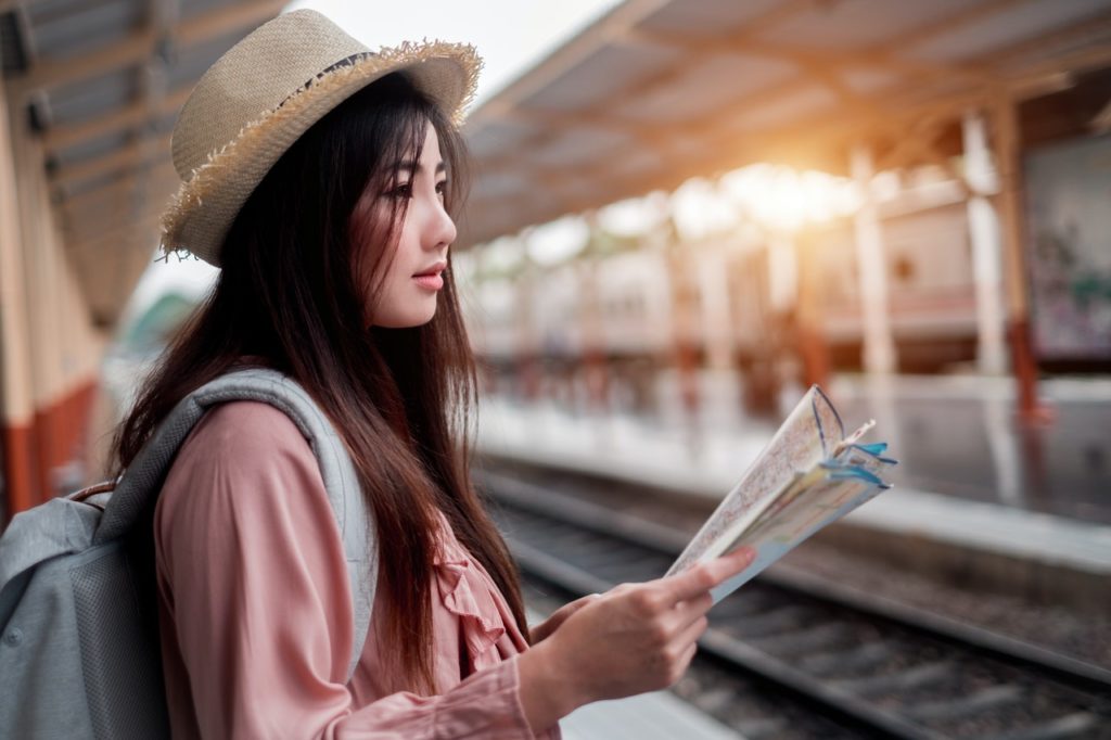 asian tourist waiting for train holding map