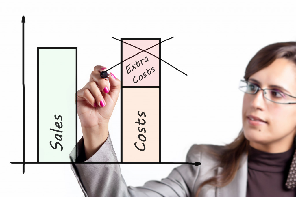 Businesswoman crossing out a drawing depicting extra costs on a transparent board.