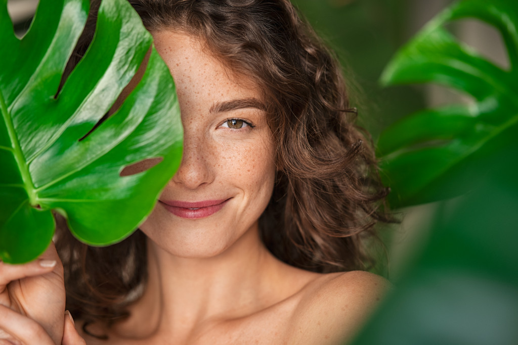 woman with curly hair and freckles behind big leaves