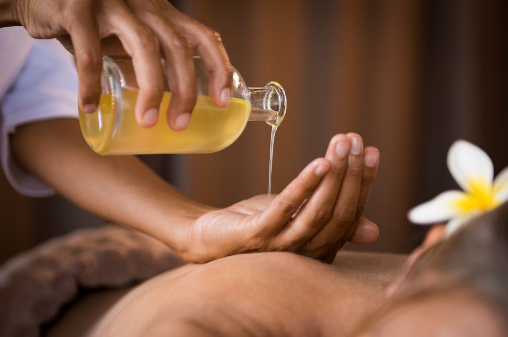 masseur hands pouring aroma oil on woman